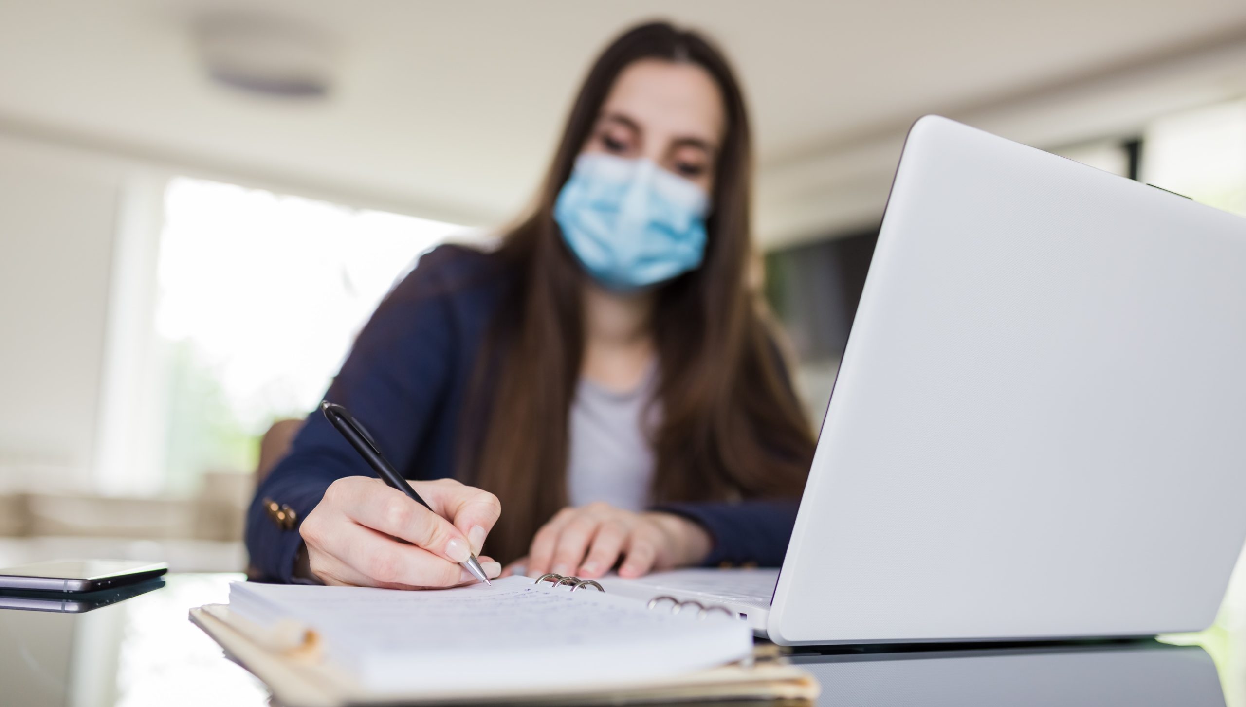 Young woman wearing medical face mask working from home. Freelancer or online learning concept during coronavirus pandemic.